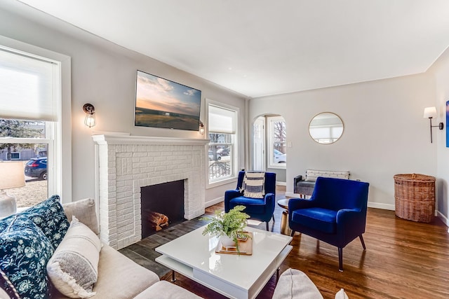 living area with a brick fireplace, baseboards, and wood finished floors