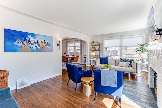 living room featuring a fireplace, wood finished floors, visible vents, and arched walkways