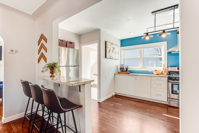 kitchen featuring a kitchen bar, light stone counters, dark wood-style floors, white cabinetry, and stainless steel appliances