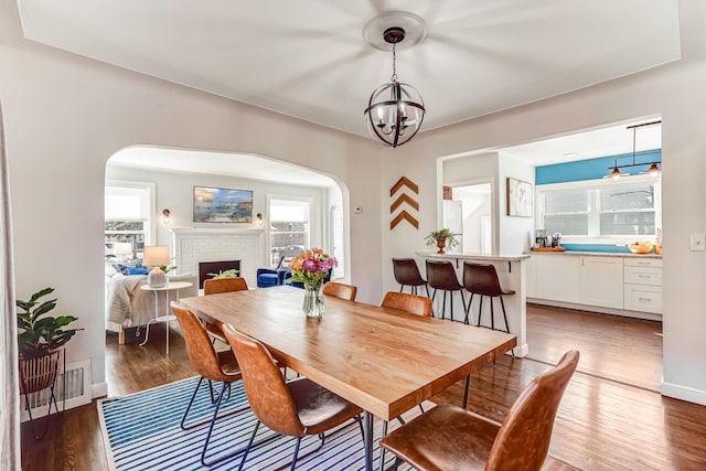 dining room with visible vents, a brick fireplace, baseboards, wood finished floors, and arched walkways