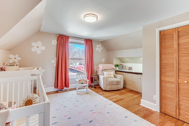 bedroom featuring visible vents, a crib, baseboards, vaulted ceiling, and wood finished floors