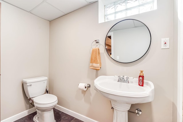 half bath with a drop ceiling, baseboards, toilet, and tile patterned flooring