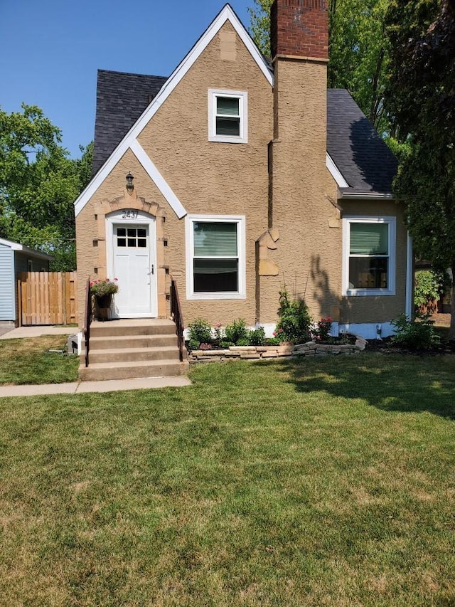 view of front of property featuring a front yard, fence, a shingled roof, stucco siding, and a chimney