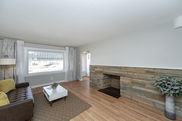 living area featuring baseboards, arched walkways, a stone fireplace, and wood finished floors