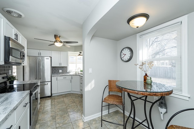 kitchen featuring visible vents, a ceiling fan, tasteful backsplash, white cabinetry, and stainless steel appliances