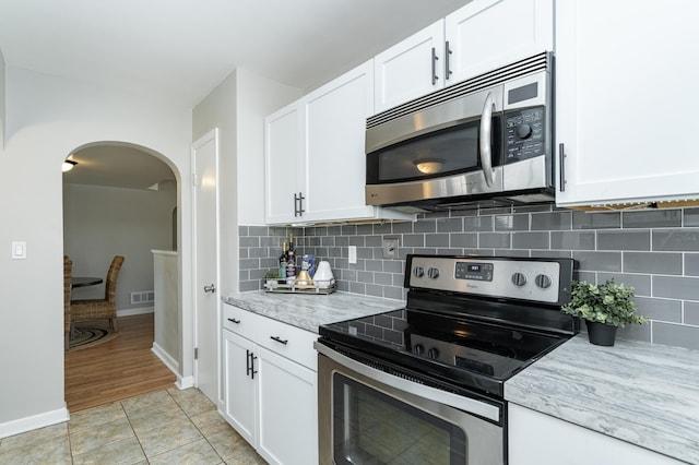 kitchen with arched walkways, decorative backsplash, appliances with stainless steel finishes, and white cabinetry