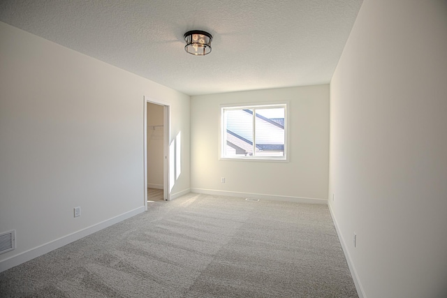 empty room featuring light colored carpet, baseboards, and a textured ceiling