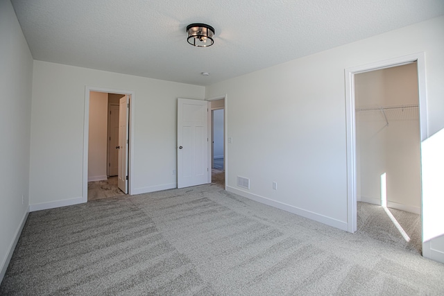 unfurnished bedroom featuring visible vents, a closet, a walk in closet, and carpet flooring