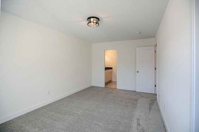 unfurnished bedroom featuring light carpet, connected bathroom, a textured ceiling, and baseboards