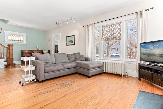 living room featuring radiator, stairs, baseboards, and wood-type flooring