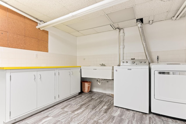 laundry room featuring a sink, cabinet space, tile walls, and independent washer and dryer