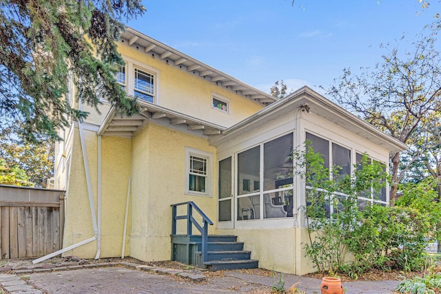 back of house featuring fence, a sunroom, and stucco siding