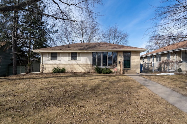 view of front facade with brick siding, entry steps, a front lawn, and fence