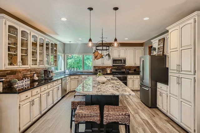 kitchen with a kitchen island, decorative backsplash, glass insert cabinets, light wood-style floors, and appliances with stainless steel finishes