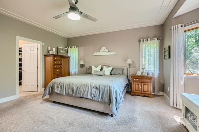 bedroom featuring a walk in closet, light colored carpet, baseboards, and ceiling fan