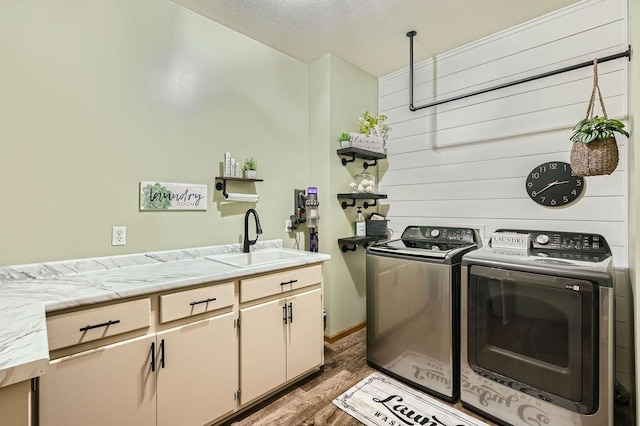 clothes washing area featuring a sink, a textured ceiling, wood finished floors, washing machine and dryer, and cabinet space