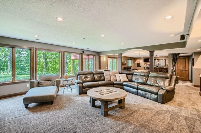 living area featuring light colored carpet, decorative columns, recessed lighting, arched walkways, and a textured ceiling