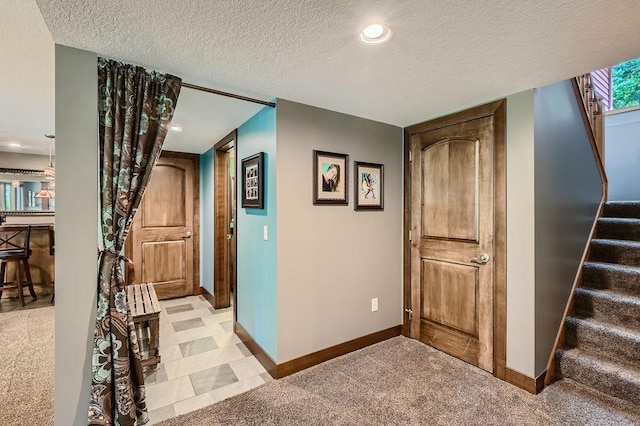 corridor with stairway, baseboards, a textured ceiling, and light colored carpet