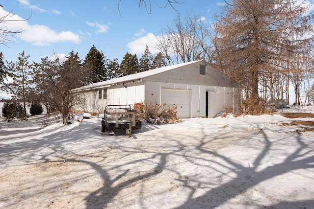 view of snowy exterior featuring a detached garage and an outbuilding