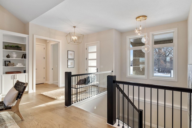 hallway featuring an upstairs landing, baseboards, an inviting chandelier, and wood finished floors