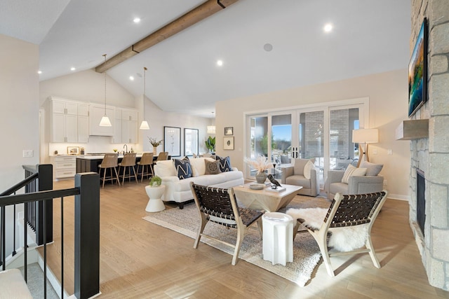 living area with beamed ceiling, high vaulted ceiling, a stone fireplace, and light wood-style flooring