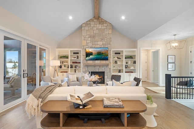 living area featuring light wood-type flooring, beam ceiling, a stone fireplace, an inviting chandelier, and high vaulted ceiling