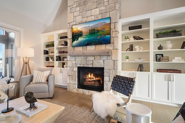 sitting room with a stone fireplace, vaulted ceiling, and wood finished floors