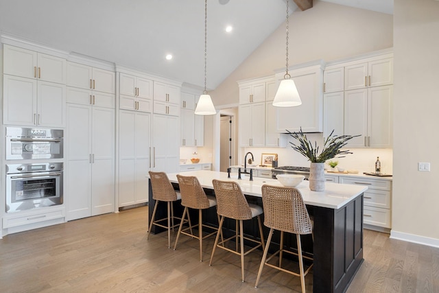 kitchen featuring light wood finished floors, light countertops, a kitchen bar, white cabinetry, and a kitchen island with sink