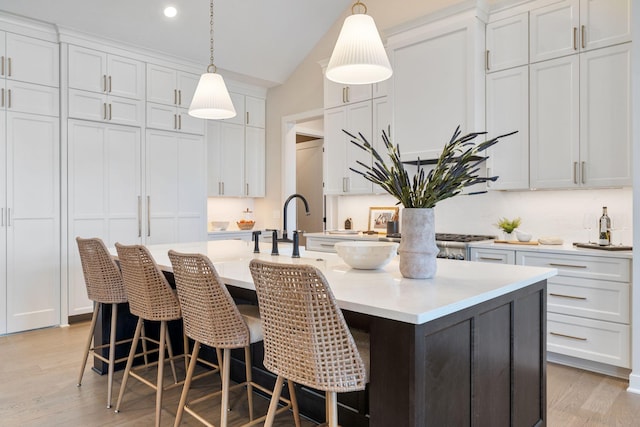 kitchen with light wood-style flooring, white cabinets, light countertops, and a kitchen island with sink