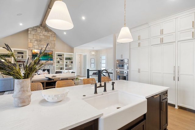 kitchen with light wood-style flooring, a fireplace, a sink, hanging light fixtures, and open floor plan