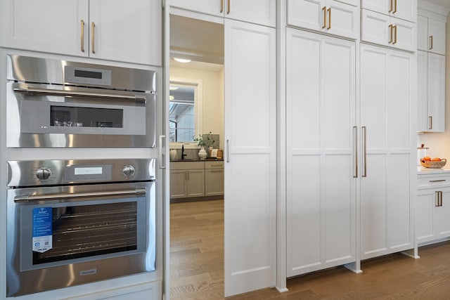 kitchen with stainless steel double oven, wood finished floors, and white cabinets