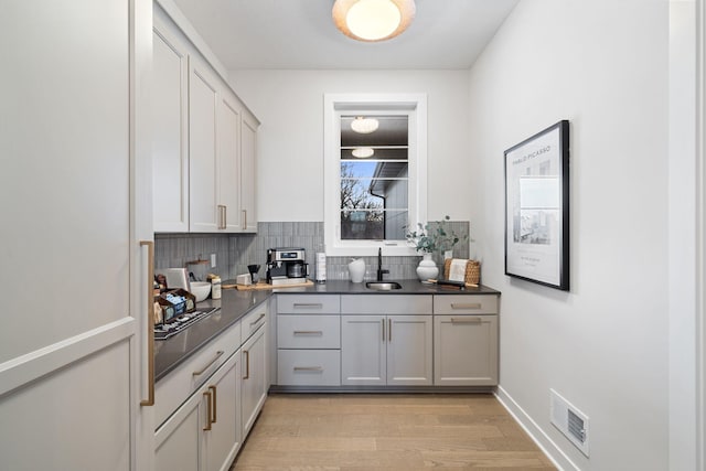 kitchen with visible vents, light wood finished floors, a sink, dark countertops, and backsplash