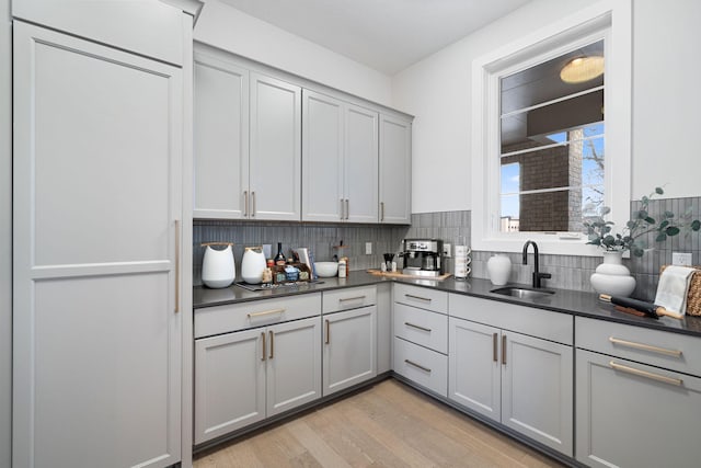 kitchen with light wood-style flooring, gray cabinets, a sink, tasteful backsplash, and dark countertops