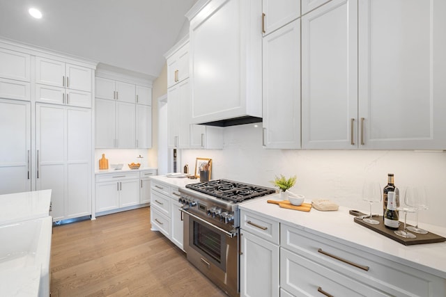 kitchen featuring high end range, white cabinetry, light wood-type flooring, and custom range hood