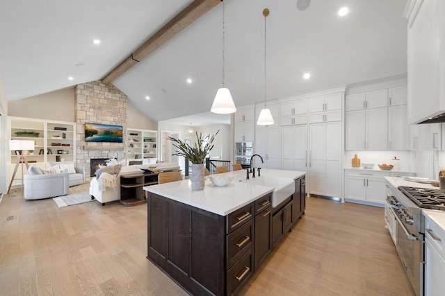 kitchen featuring a stone fireplace, white cabinets, light wood-type flooring, and a sink