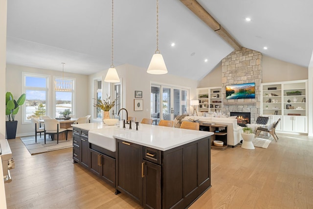 kitchen with a sink, beam ceiling, a stone fireplace, and light wood finished floors