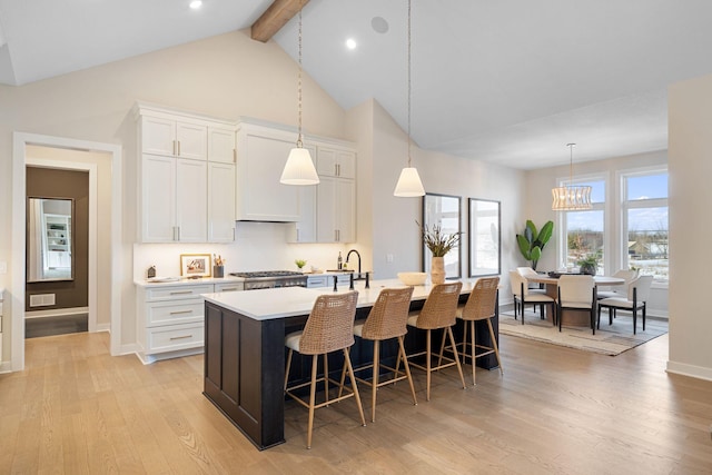 kitchen featuring light wood-type flooring, beamed ceiling, an island with sink, a kitchen breakfast bar, and light countertops