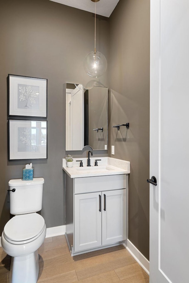 bathroom with vanity, toilet, wood finished floors, and baseboards