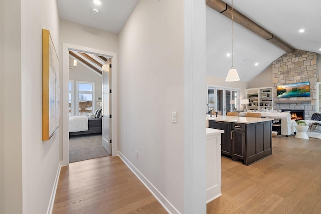 hallway with vaulted ceiling with beams, light wood-style floors, and baseboards