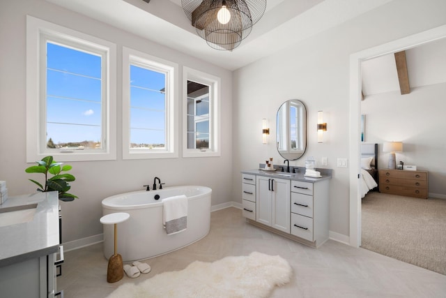 ensuite bathroom with beamed ceiling, ensuite bathroom, baseboards, a soaking tub, and vanity