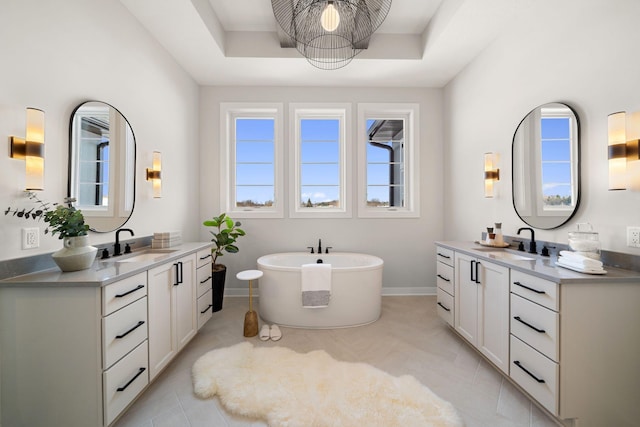 bathroom with a freestanding bath, a raised ceiling, two vanities, and a sink