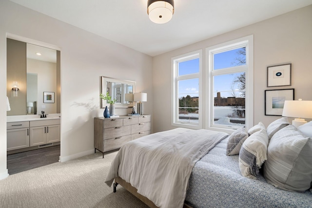 bedroom featuring light colored carpet, baseboards, ensuite bathroom, and a sink