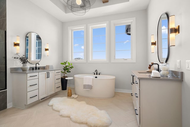 full bath with a sink, baseboards, a freestanding bath, and two vanities