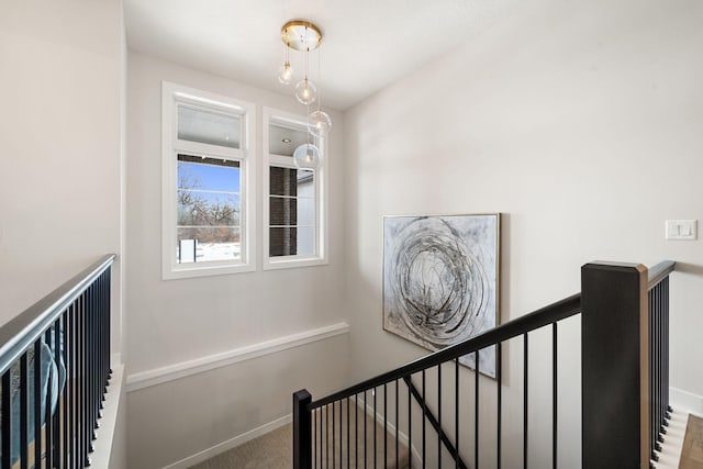 hallway with an upstairs landing, baseboards, and carpet floors