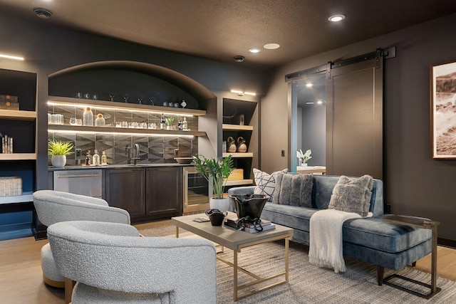 interior space with built in shelves, light wood-style flooring, a textured ceiling, a barn door, and indoor wet bar