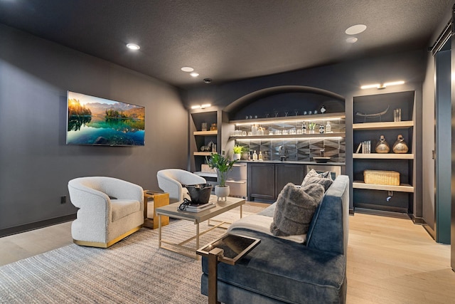 living area with recessed lighting, light wood-style flooring, a textured ceiling, and bar area