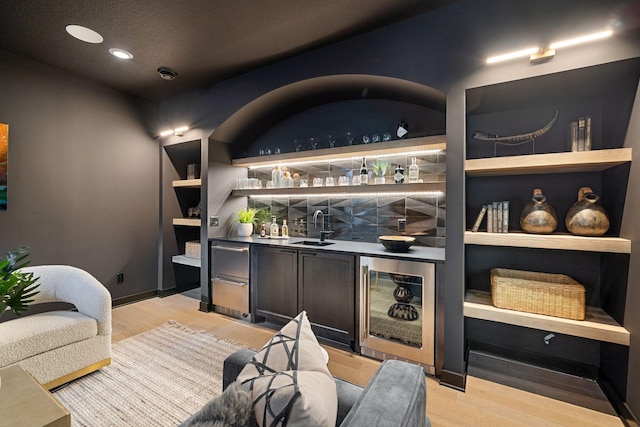 bar with wet bar, beverage cooler, light wood-type flooring, and a sink