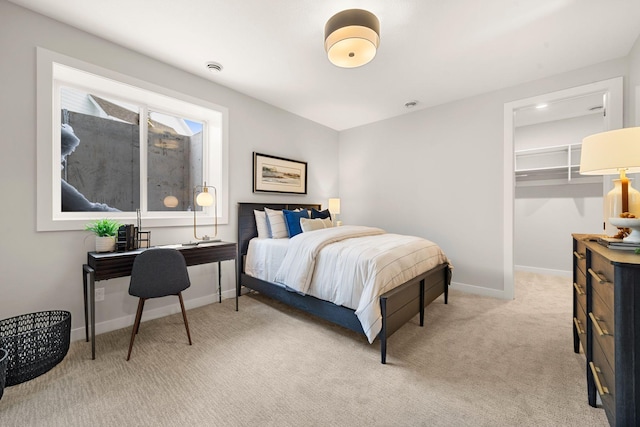 bedroom featuring light colored carpet, a walk in closet, and baseboards