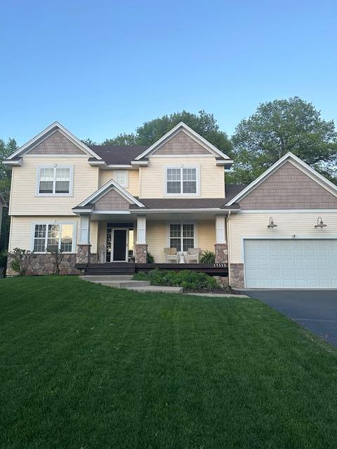 craftsman-style home featuring aphalt driveway, stone siding, an attached garage, and a front yard