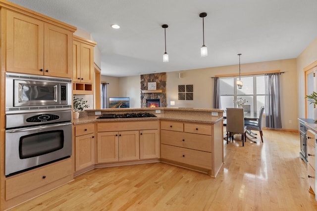 kitchen with a peninsula, light brown cabinetry, stainless steel appliances, pendant lighting, and light wood-type flooring